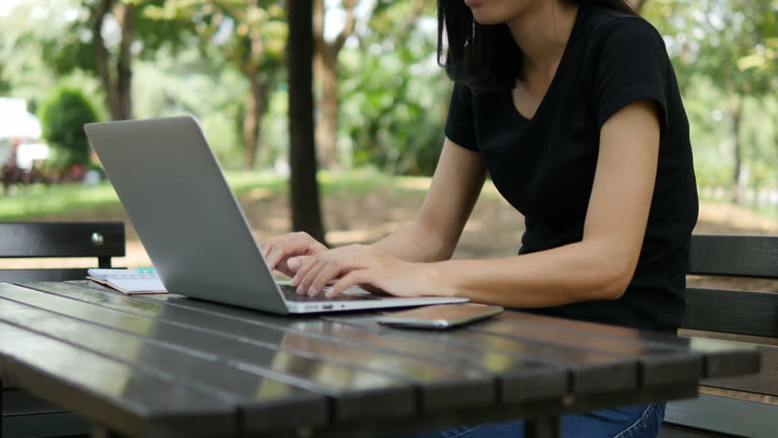 4K: Asian woman working on modern laptop in the park.