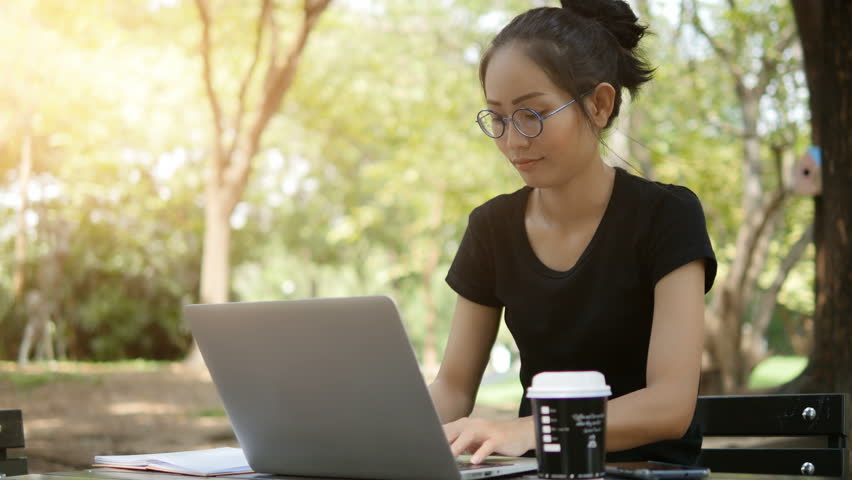 4K: Asian woman working on modern laptop in the park.