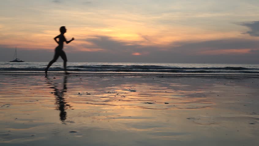 Young woman jogging on the beach at sunset (HD)