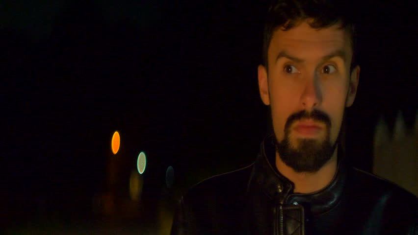 The man with a beard stand on the road. night time. anamorphic lens shot