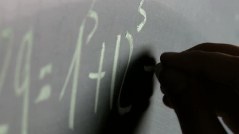 Teacher's hand writing math formula on a clean blackboard at school close up