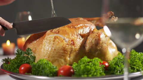 Thanksgiving or Christmas turkey dinner. Carving the turkey in slow motion cutting juicy breast meat. Whole roasted turkey steaming on tray garnished with tomatoes and herbs. Stock Video
