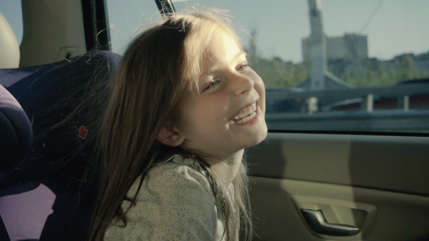 Happy funny girl in a car. Little girl in back seat looking through the window