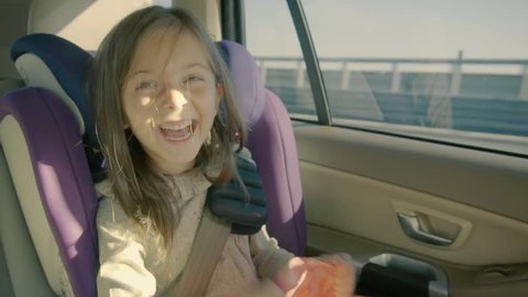 Cute little girl riding in the car at back seat and looking happy.