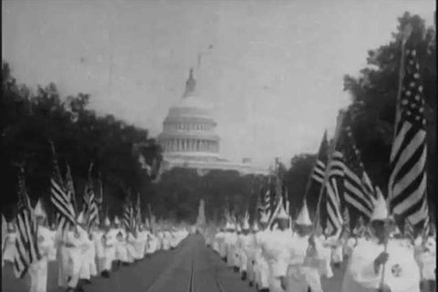 CIRCA 1920s - Members of the Ku Klux Klan, wearing glory suits, parade, with American flags, crosses and a Klansman dressed as Uncle Sam, through Washington, D.C., in 1928.