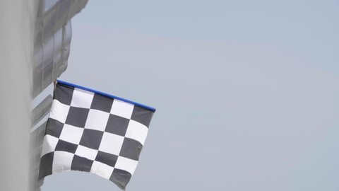 Man holding and waving Checkered race flag in slow motion at finish line on a raceway. 