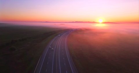 Amazing aerial view of the road with driving cars, morning fields and forests covered with fog and rising sun. Russia
