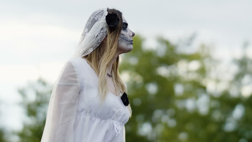The portrait of young woman with spooky make-up for Halloween in a white bride dress. 4K