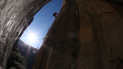 A silhouette of a female rock climber with safety harness and rope attempts to climb a boulder during the day in a national park