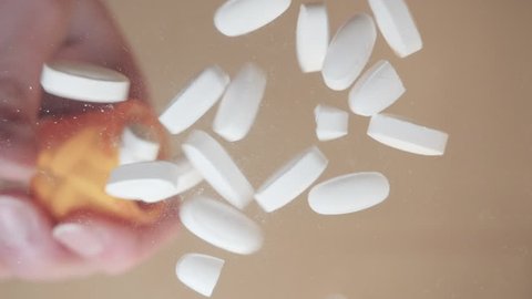 White prescription pills fall directly onto the lens in slow motion. The pain killer tablets represent pharmaceutical substance abuse in teens and recreational drug use of opiates.