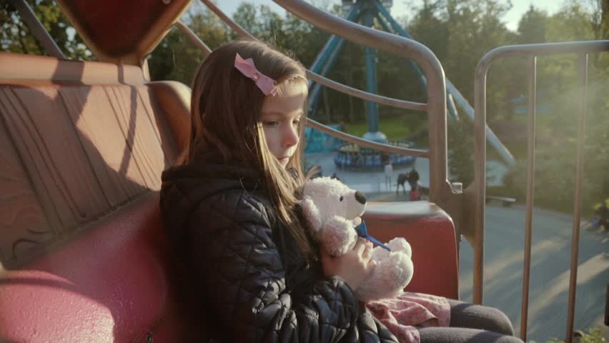 Girl with teddy bear in the amusement park in kids train. Children outdoors.