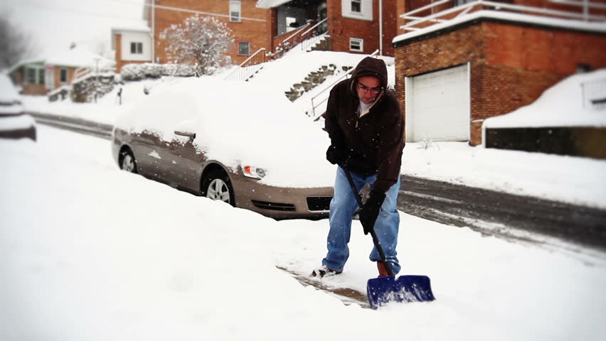 A man shovels the sidewalk outside his house in a snow storm.