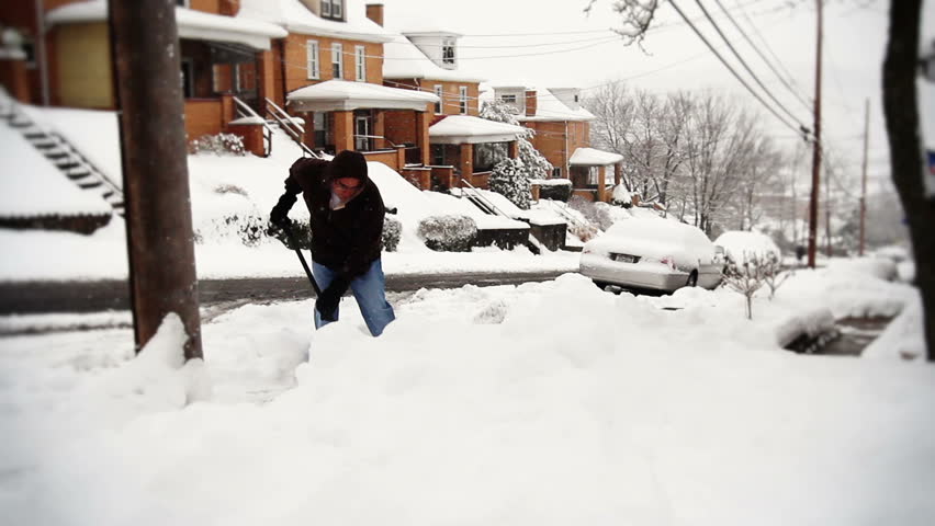 A man shovels the sidewalk outside his house in a snow storm.