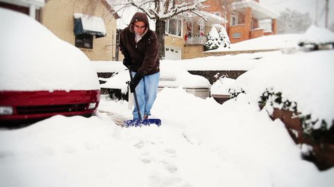 A man shovels his driveway in a snow storm.