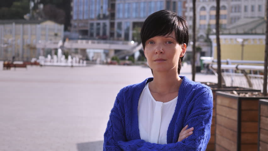 Young brunette is standing on the street and is smiling at the camera