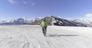 forward aerial over biker man cycling on snowy path during winter with mtb e-bike. Cyclist on bike on snow outdoors in winter. 4k drone flight video