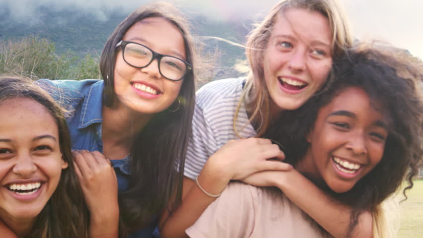 Four happy teenage girls piggybacking outdoors, close up