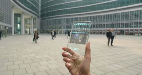 A subjective perspective, a hand that uses a futuristic phone and thanks to holography follows a conference on business and finance. Concept of: augmented reality, future, technology