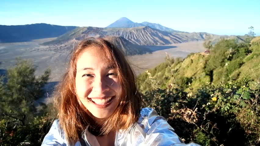 Cheerful enthusiastic Asian tourist girl happily turn around in Bromo Tengger Semeru National Park, East Java, Indonesia. Young woman have fun sightseeing with volcano, desert, and sky. (Selfie shot) Royalty-Free Stock Footage #31950964