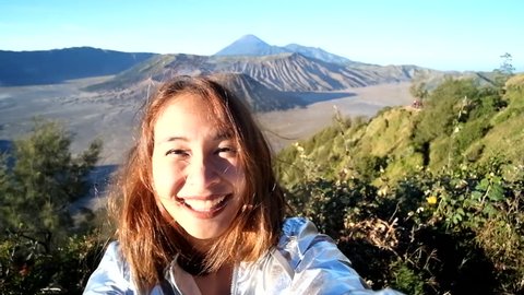 Cheerful enthusiastic Asian tourist girl happily turn around in Bromo Tengger Semeru National Park, East Java, Indonesia. Young woman have fun sightseeing with volcano, desert, and sky. (Selfie shot)