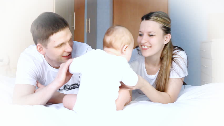 Happiness family: father, mother and baby playful on the bedroom