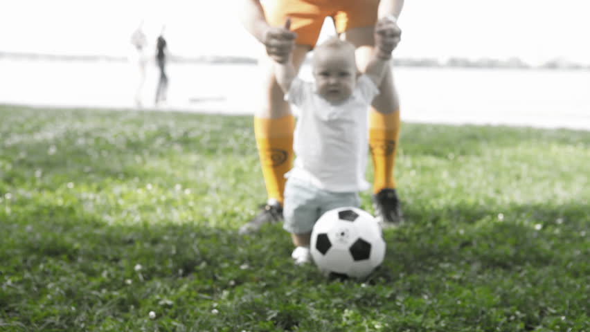 Baby with father playing with soccer ball on the grass