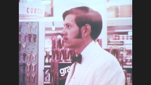 1970s: Teenager stands at check out counter, clerk sides beer back to teenager. Teenager smiles.