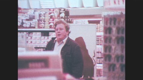 1970s: Teenager sets money on check out counter, points to beer, smiles, walks out of store. Boy runs to car, clerk chases boy. Teenager puts beer on counter, hides face from clerk under cowboy hat.