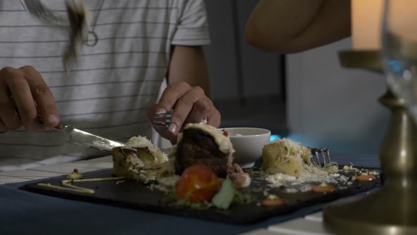 Closeup of man cutting meat on the plate and offering it to his girlfriend for tasting it in a restaurant