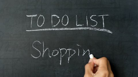 Female hand writing "to do list : shopping" on chalk board 