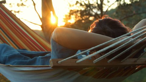 Woman lies in a hammock and enjoys the sunset