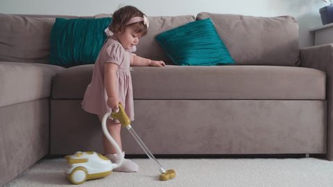 Cute little baby girl using toy vacuum cleaner in room