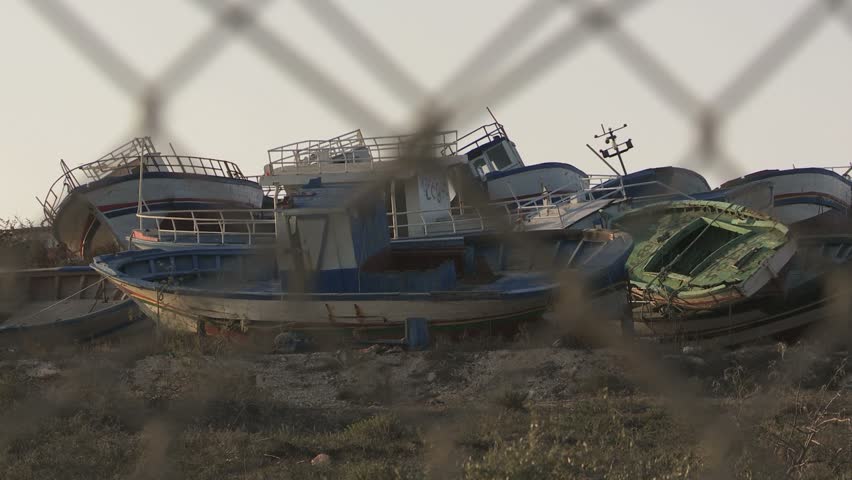Ship graveyard in Lampedusa. Abandoned ships of immigrants from Africa behind fence in the refugees camp 2