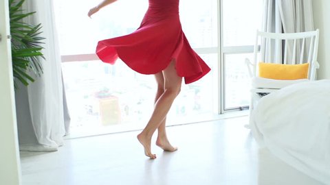 Woman in dress dancing and turning around by window at home

