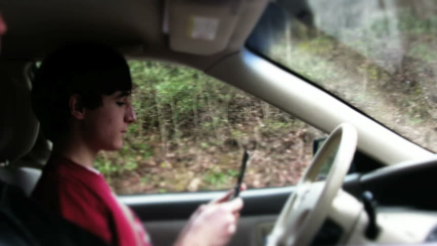 Young teen texting and driving car. Teen youth using smartphone while driving car. Reckless teen texting and driving car. bad driving habits while using phone. Accident waiting to happen.