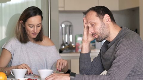 Bored, offended couple eating breakfast in kitchen at home

