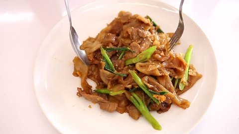 Stir fried flat noodle and pork with preserved soy bean paste in white on wooden table. Thai style food