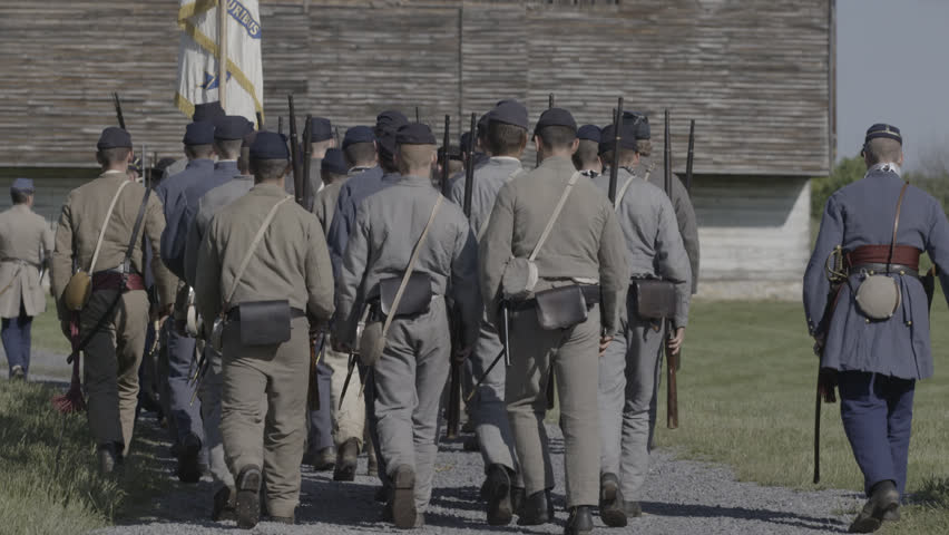 VIRGINIA - MAY 2017 - large-scale, epic Civil War anniversary reenactment -- march to battle. Young Confederates marching past snake-rail fences and across tall grass field with flags and muskets