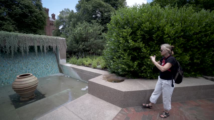 Pretty, mature woman taking a photo with her smart phone in the garden outside the Smithsonian Institution Castle and Arts and Industries buildings on the National Mall in Washington