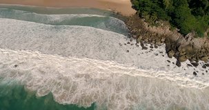 Aerial drone view of beautiful tropical island beach and waves crashing coastline cliff during sunny summer day - video in slow motion