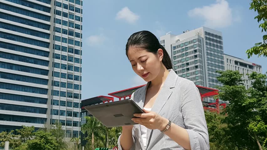professioan Asian business woman using the mobile touch pad digital tablet on the road, financial center building on the background.