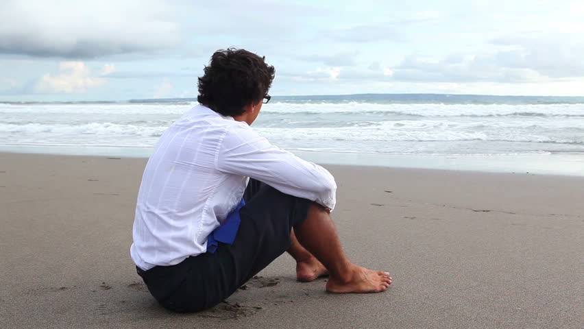 young man in office clothes sitting on the beach then standing