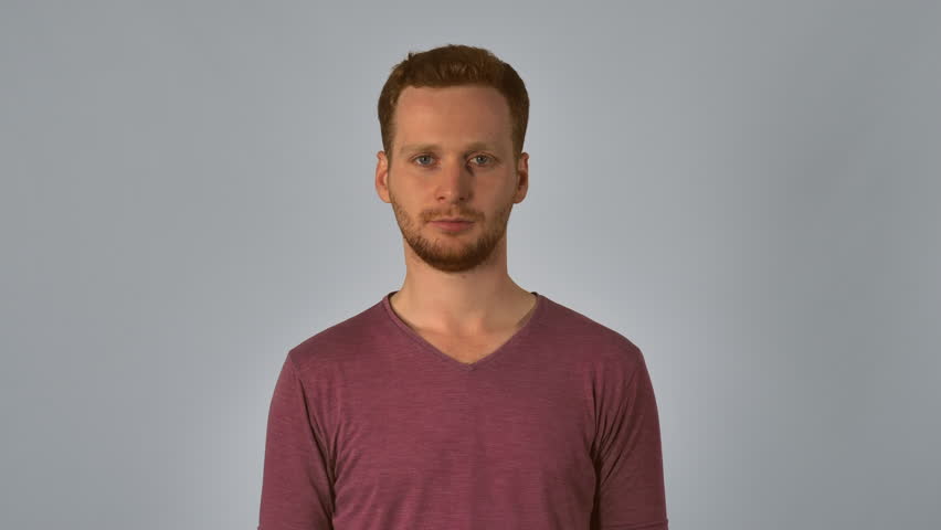 caucasian guy with red hair posing showing hand gesture puts his hands to ear and listening. handsome redhead men wearing in casual t-shirt. portrait young caucasian man on grey background