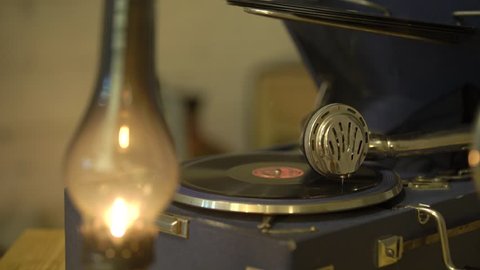 Gramophone with a vinyl record in a retro interior, a kerosene lamp is burning. Phonograph plays old music song on vinyl plate