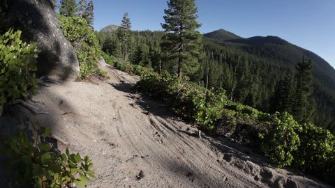 A mountain biker speeds down a dirt trail during the day, kicking up a dirt cloud, filmed at the Lake Tahoe National Park in HD with some lens flare