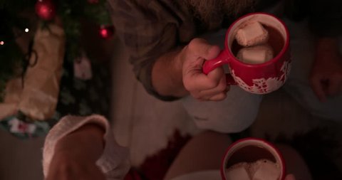 Mature redhead couple celebrating Christmas drinking hot chocolate and sitting on floor under Christmas tree : vidéo de stock