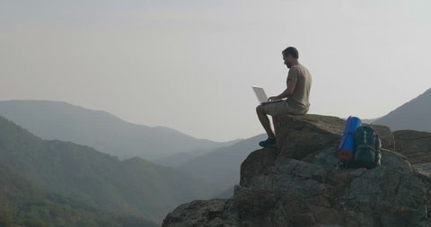 A man uses computer on top of a mountain and behind a magnificent landscape. Concept of: unlimited internet surfing, freedom, unlimited technologies.