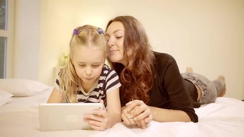 Beautiful Mother and Her Little Daughter Have Good Time Reading Children's Books on a Tablet Computer.