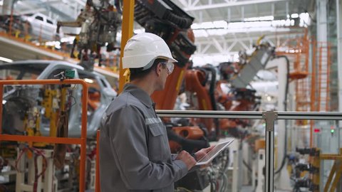 Automobile plant, modern production of cars, robot equipment, working man checks data on the tablet.