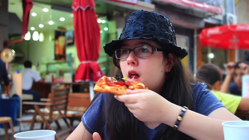 Child with eye glasses enjoying pizza in cafeteria. 